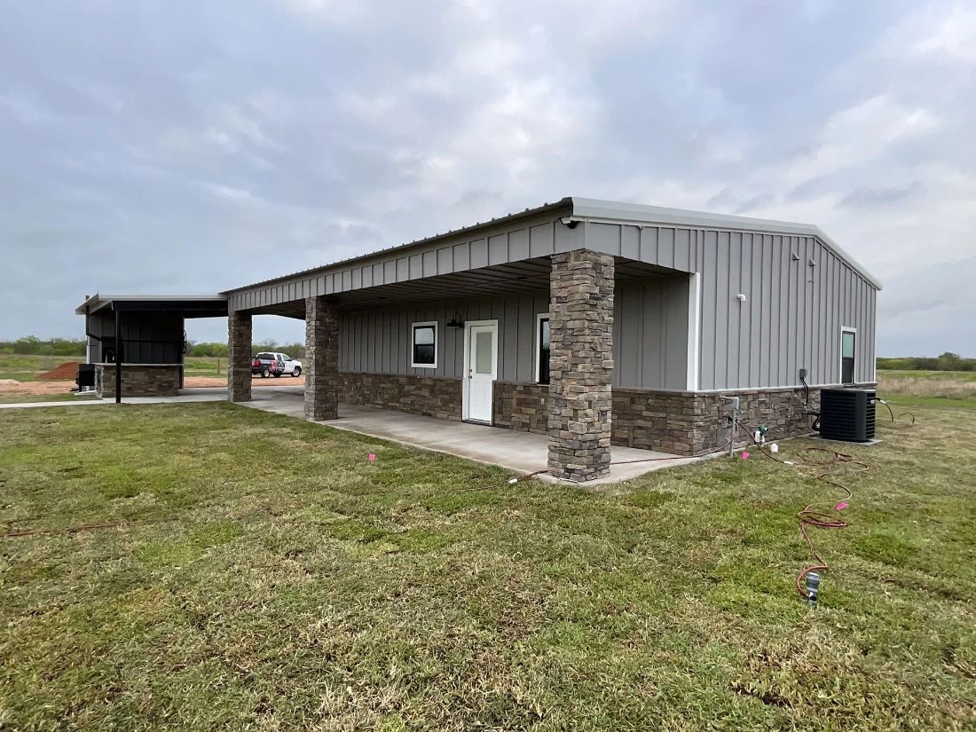 Gray metal barndominium with stone columns and carport